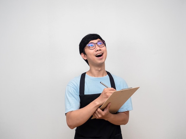 Asian man wearing apron gentle smile holding check list board looking above