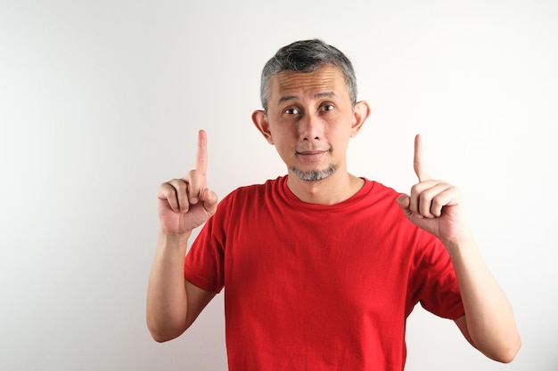 Asian man wearing casual clothes pointing fingers up at copy space isolated over white background