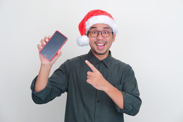 Asian man wearing Christmas hat showing empty handphone screen with joyful expression