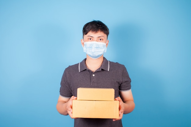 Asian man wearing a mask delivers express delivery boxes on blue background