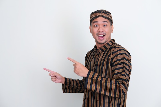 Asian man wearing traditional Javanese costume pointing to right side with wow expression