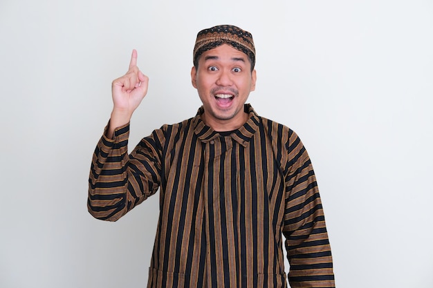 Asian man wearing traditional Javanese costume pointing up with excited expression