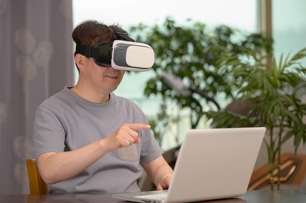 Asian man wearing VR headset and using laptop while sitting at his desk