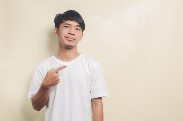 Asian man wearing white tshirt pointing to empty space on isolated background