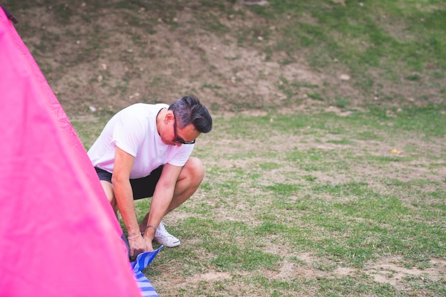 an Asian man in white t shirt setting pink tent at campground