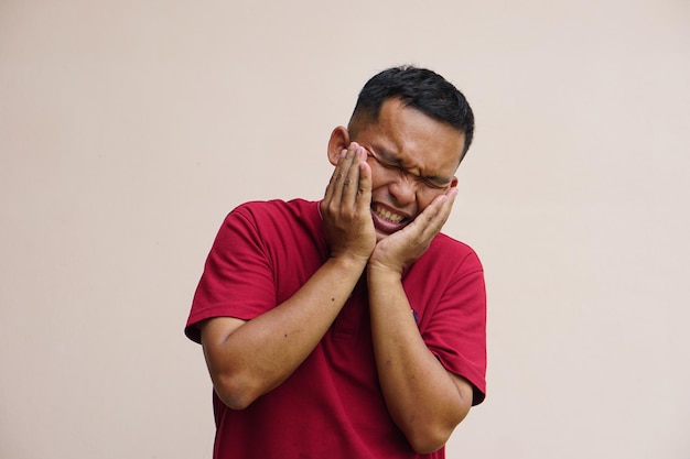 Asian man with toothache touches cheek with her hand