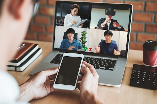 Asian man working from home use Smart working and video conference online meeting with Asian team using laptop and tablet online in video call for new projects