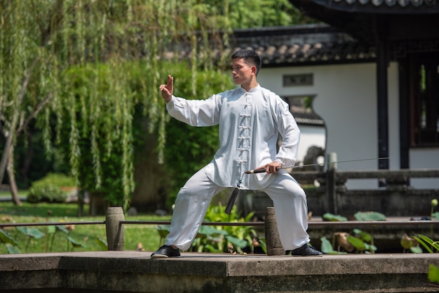 Asian man working out with Tai Chi sword in the morning at the park, Chinese martial arts