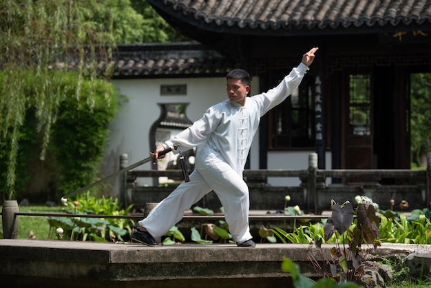 Asian man working out with Tai Chi sword in the morning at the park, Chinese martial arts