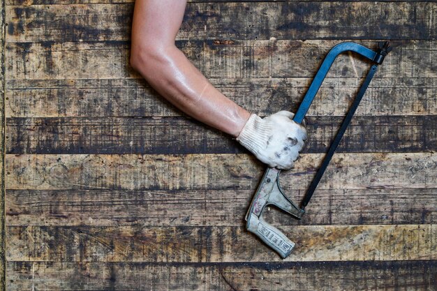 Photo asian mechanic holds a hacksaw on a wooden background