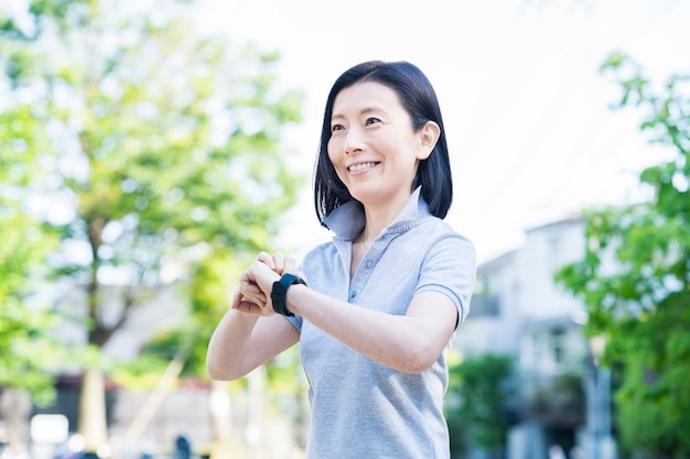 Asian middle-aged woman operating a smartwatch outdoors