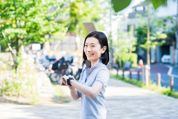 Asian middle-aged woman operating a smartwatch outdoors