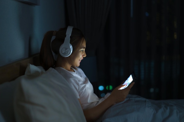 Asian mobile addict woman using digital tablet browsing the internet for watching movie or virtual meeting video call online with boyfriend on the bed before she sleeping at night.