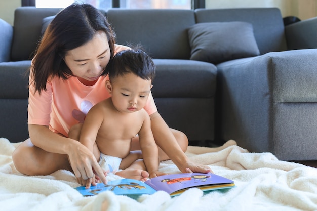 Asian mom teaching and reading book with her cute baby boy at home. Family and togetherness concept