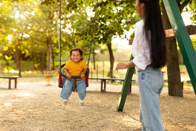 Asian mommy swinging baby daughter on swing outdoors in park