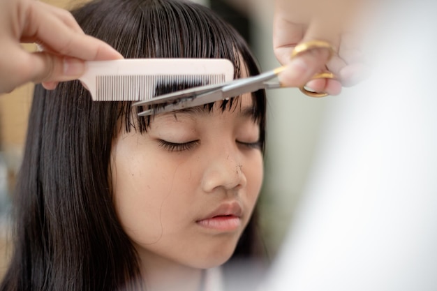 Asian Mother cutting hair to her daughter in living room at home while stay at home safe from Covid19 Coronavirus during lockdown Selfquarantine and social distancing concept