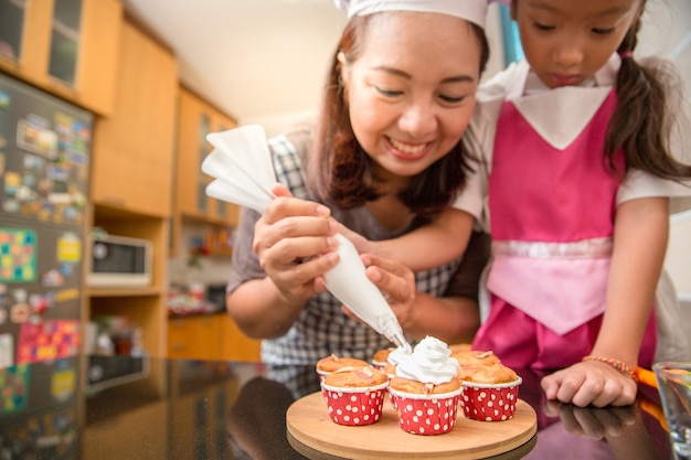 Asian mother and daughter enjoy making and decorate bakery cake in real life kitchen