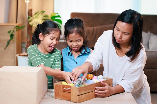 Asian mother and her daughters are playing with baby bunny and decorating easter eggs preparing for Easter at home Happy family Happy easter Happy holiday