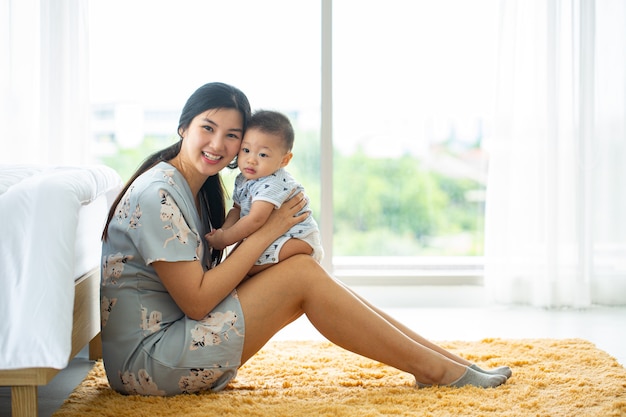 Asian mother holding her baby beside bedroom.