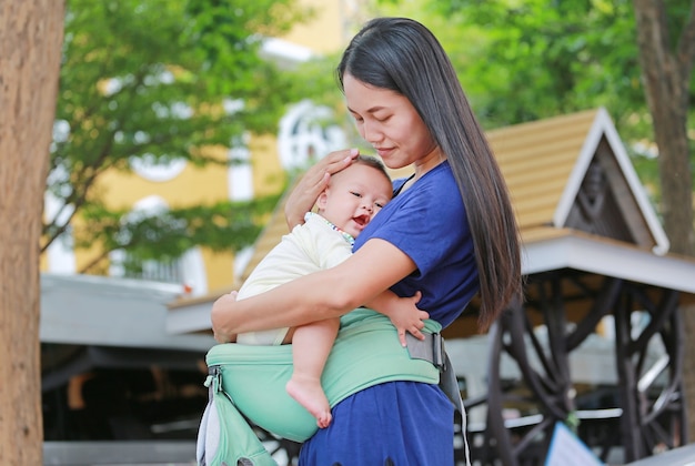 Asian mother hugging her infant on ergonomic baby carrier.