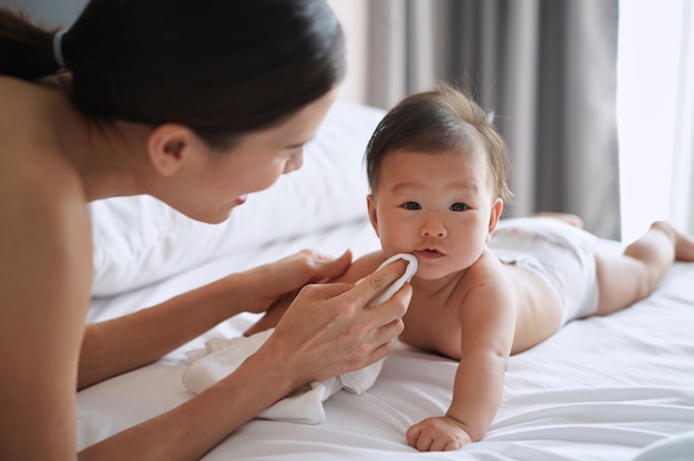 Asian mother is wiping her newborn baby mouth gently by cloth diaper.