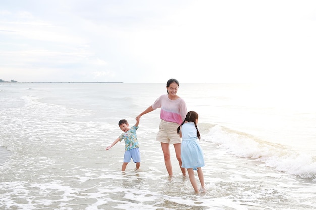 Asian mother and kids enjoy playing on tropical sand beach at sunrise Happy family mom and child having fun in summer holiday