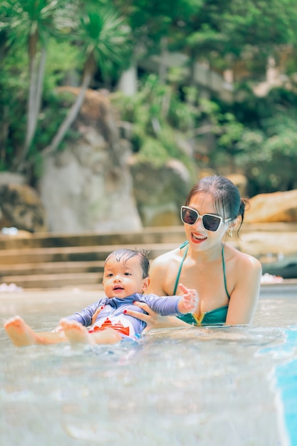 Asian mother and little son enjoying swimming in a swimming pool in summer vacation