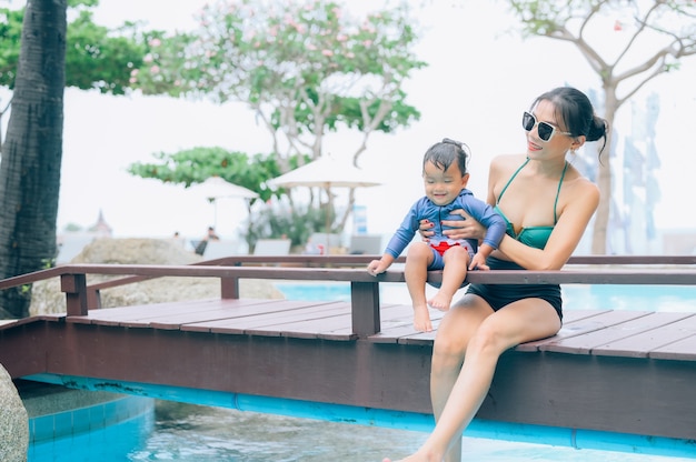 Asian mother and little son enjoying swimming in a swimming pool in summer vacation