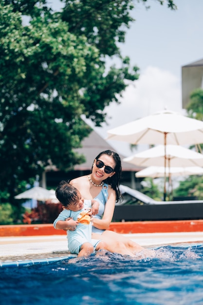 Asian mother and little son enjoying swimming in a swimming pool in summer vacation.