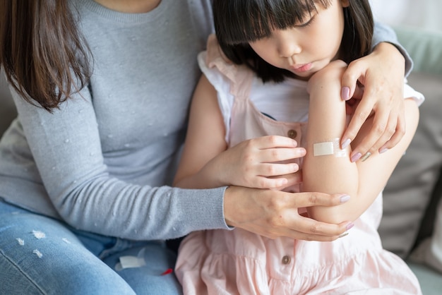 Asian mother putting court plaster adhesive bandage onto her daughter at home