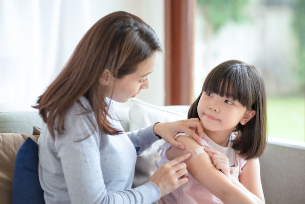 Asian mother putting court plaster adhesive bandage onto her daughter at home