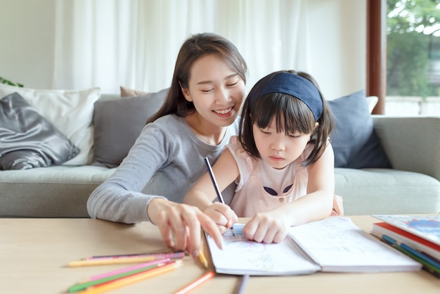 Asian mother teaching her cute kid daughter to studying in living room at home