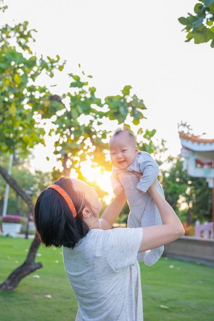 Asian mother throws baby up, laughing and playing in the park