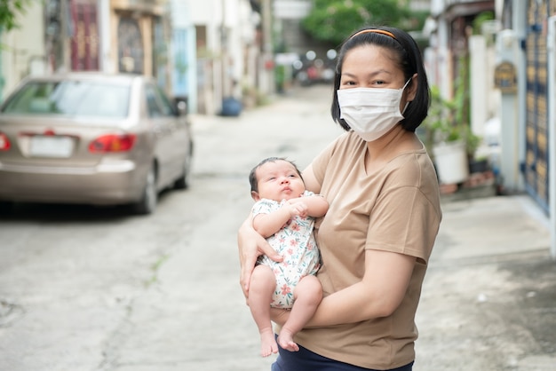 Asian mother wearing surgical face mask holding her baby, COVID-19 concept