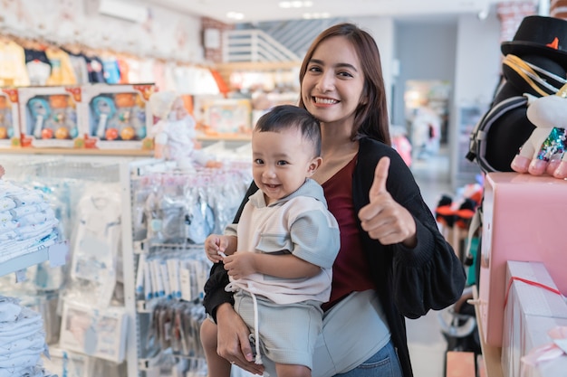 Asian mother with her toddler boy shopping in the baby shop with thumb up