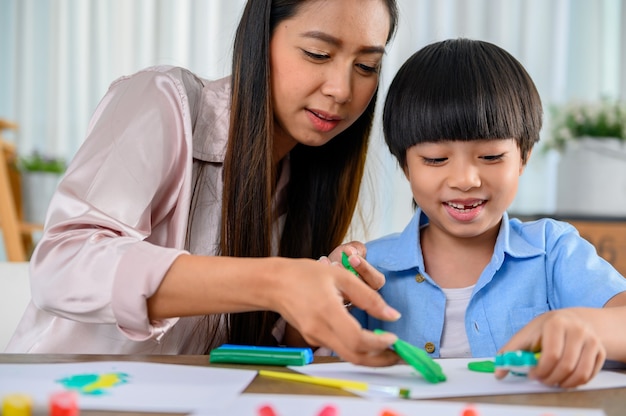 Asian mother work home together with son. Mom and kid play dough. Child creating plasticine clay model. Woman lifestyle and family activity.