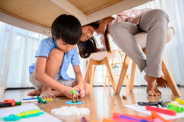 Asian mother work home together with son. Mom online working and kid play dough under table. Woman lifestyle and family activity.