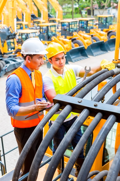 Asian motor mechanic discussing with engineer task list in construction machine workshop