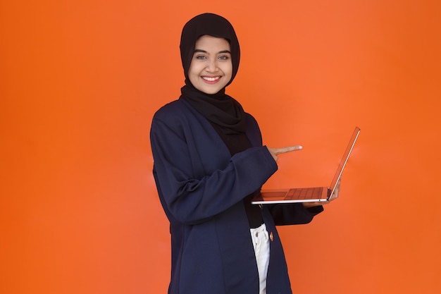 Asian muslim business lady in formal wear looking at camera while pointing to pc laptop