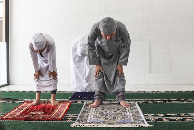 Asian muslim family are kneeling and praying salah together at mosque