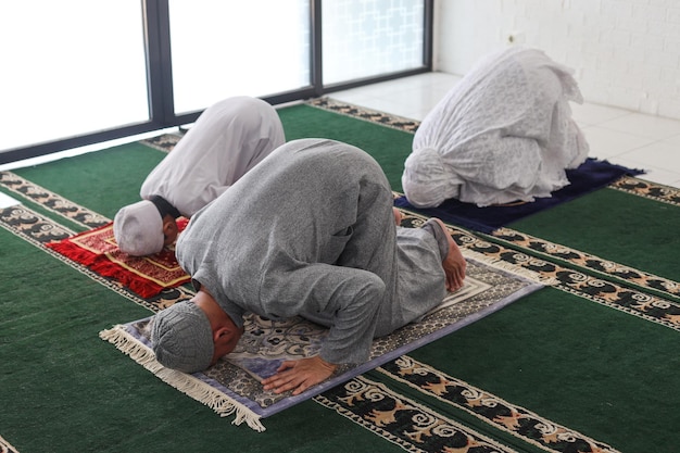 Photo asian muslim family praying jamaah together and doing sujud movement or called a sajdah