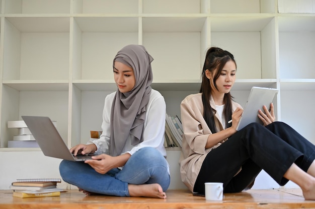 Asian Muslim female and her friend focused using their laptop and tablet