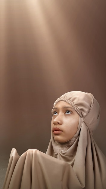 Asian Muslim girl in a hijab raising her hands and praying