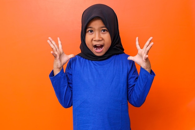 Asian muslim girl wearing hijab screaming against orange background