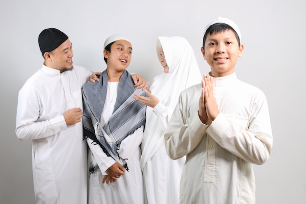 Asian muslim kid in skullcap showing greeting hands gesture with his family on the background