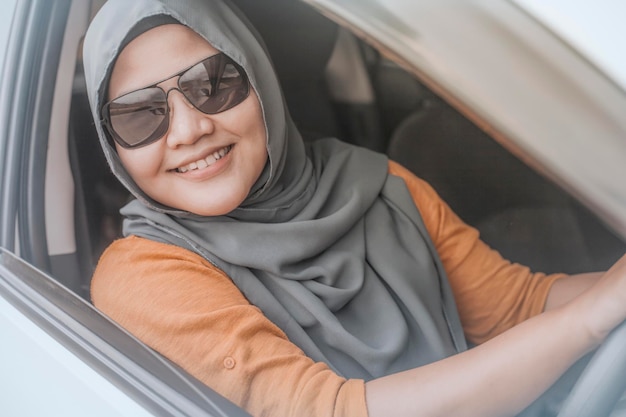 Asian muslim lady smiling while driving having fun leisure in vacation trip car ride sharing concept