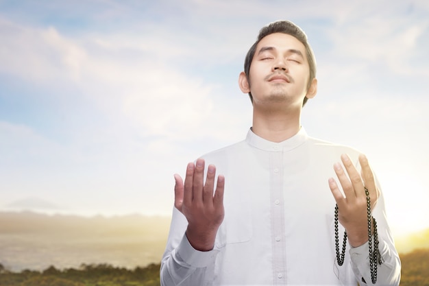 Asian Muslim man praying with prayer beads on his hands