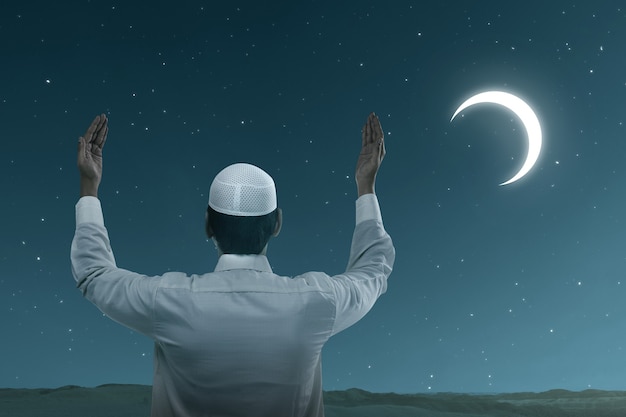 Asian Muslim man standing while raised hands and praying with the night scene