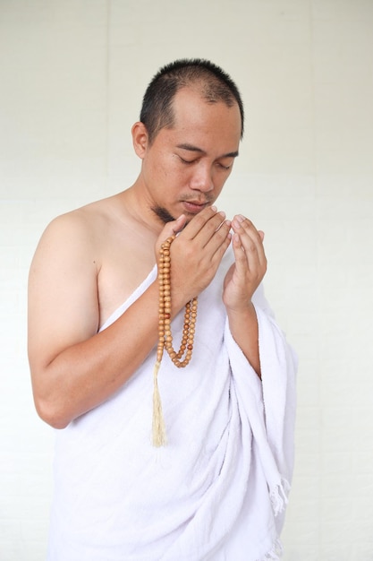 Asian muslim man wearing white ihram clothes and praying while holding prayer beads