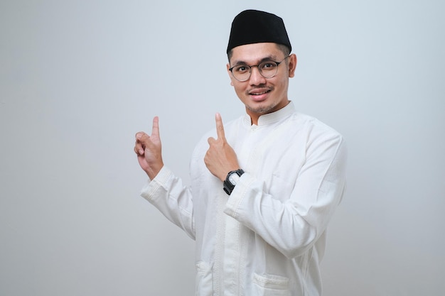 Asian muslim mas pointing something on his side with his both hand over white background